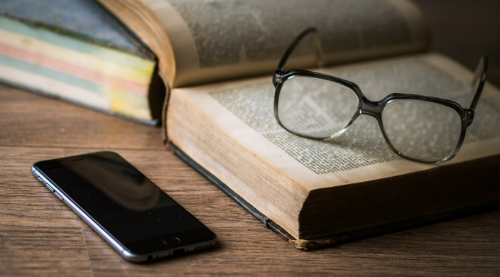 open book with a pair of glasses on the page; cell phone on table next to book